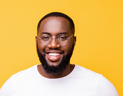 Een zwarte man met een bril en een baard die lacht tegen een gele achtergrond.