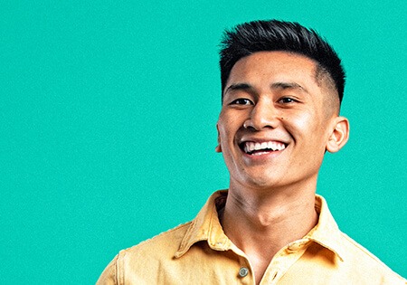 Um homem asiático sorridente com uma camisa amarela.