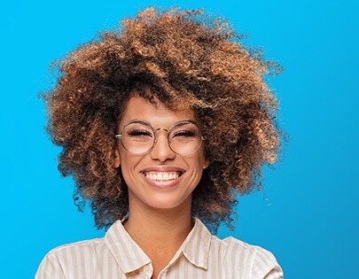 Eine Frau mit Afro-Haaren und Brille lächelt auf blauem Hintergrund.