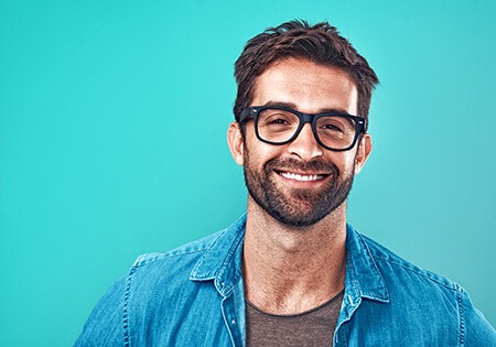 Un homme à lunettes souriant sur fond turquoise.